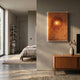 A modern, sunlit bedroom with neutral tones features a neatly made bed, wooden console with dried flowers, and the Lumora Amber Orange Acrylic Framed 3D Paper Wall Art by Giant Sculptures glowing on the wall. Shelving and a large window appear in the background.