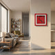 A modern living room features a sofa, armchair, bookshelf, and large window. The Cavendro Single Dark Cigar Framed Wall Art by Giant Sculptures adds bold decor to the white wall dividing the living area and kitchen.