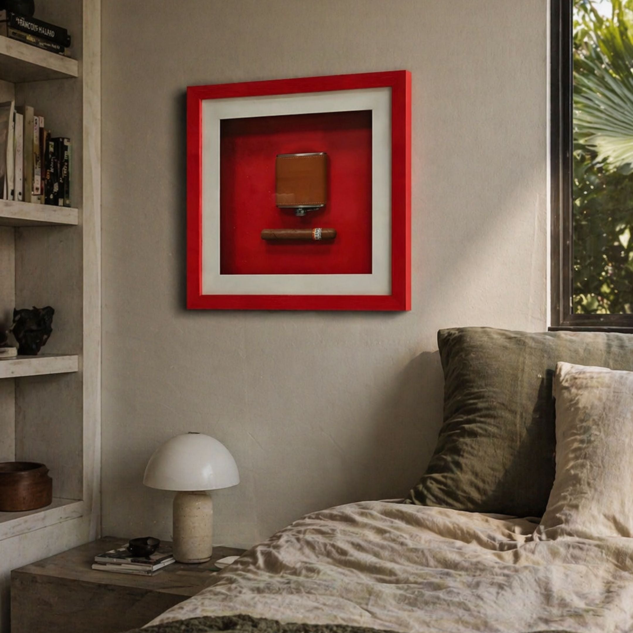 A cozy bedroom features a bed with green and beige pillows, a small white lamp on the bedside table, and the Cavendro Brown Flask & Cigar Framed Wall Art by Giant Sculptures above. Sunlight streams in, highlighting lush greenery outside the window.