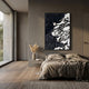 A modern, minimalist bedroom features a low bed, neutral bedding, and the Nivoria III Black & White Textured Abstract 3D Wall Art by Giant Sculptures above the headboard. Large windows fill the space with light, and a vase with dried grasses sits on a floating nightstand.