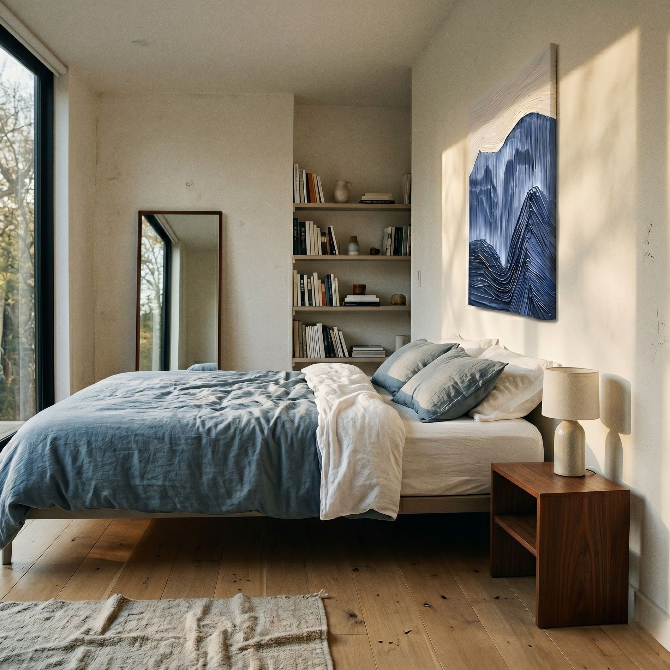 A modern, minimalist bedroom features a large bed with blue and white bedding, a wooden nightstand with two lamps, bookshelf, tall mirror, and the Terralune Blue Layered Ridge 3D Wall Art by Giant Sculptures above the bed. Sunlight pours in from floor-to-ceiling windows.