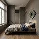 Minimalist bedroom with a low bed, neutral bedding, wooden floor, gray walls, and Aurevion Green Radiant Eye 3D Wall Art by Giant Sculptures as a striking accent. A twig-filled vase sits on the window ledge near a corner chair lit by large windows.