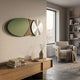 Modern living room with a large window, beige armchair, throw blanket, built-in shelves, and minimalist decor. Above a wooden console hangs the Aurelune Olive & Brown Silver Metal Disc 3D Wall Art by Giant Sculptures for a striking focal point.