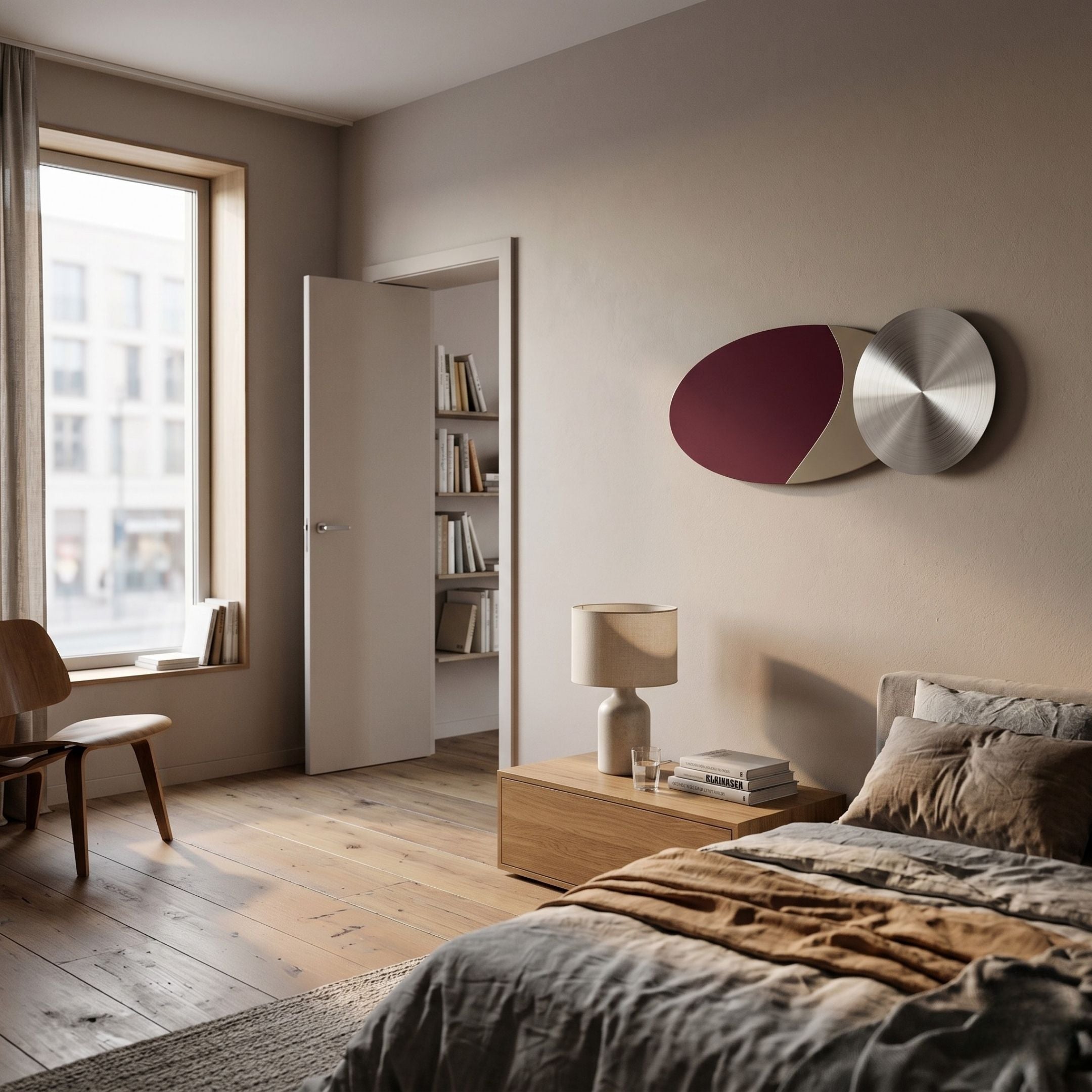 A modern bedroom with a large window, wooden floor, neatly made bed, bedside table with lamp and books, a wooden chair, bookshelf in the doorway, and Giant Sculptures' Aurelune Burgundy & Taupe Silver Metal Disc 3D Wall Art above the nightstand.
