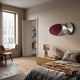 A modern bedroom with a large window, wooden floor, neatly made bed, bedside table with lamp and books, a wooden chair, bookshelf in the doorway, and Giant Sculptures' Aurelune Burgundy & Taupe Silver Metal Disc 3D Wall Art above the nightstand.
