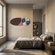 Minimalist bedroom with a large bed, gray bedding, a wooden nightstand, and bookshelf. Sunlight streams through a large window, highlighting the Giant Sculptures Aurelune Cocoa & Rose Silver Metal Disc 3D Wall Art on the wall.
