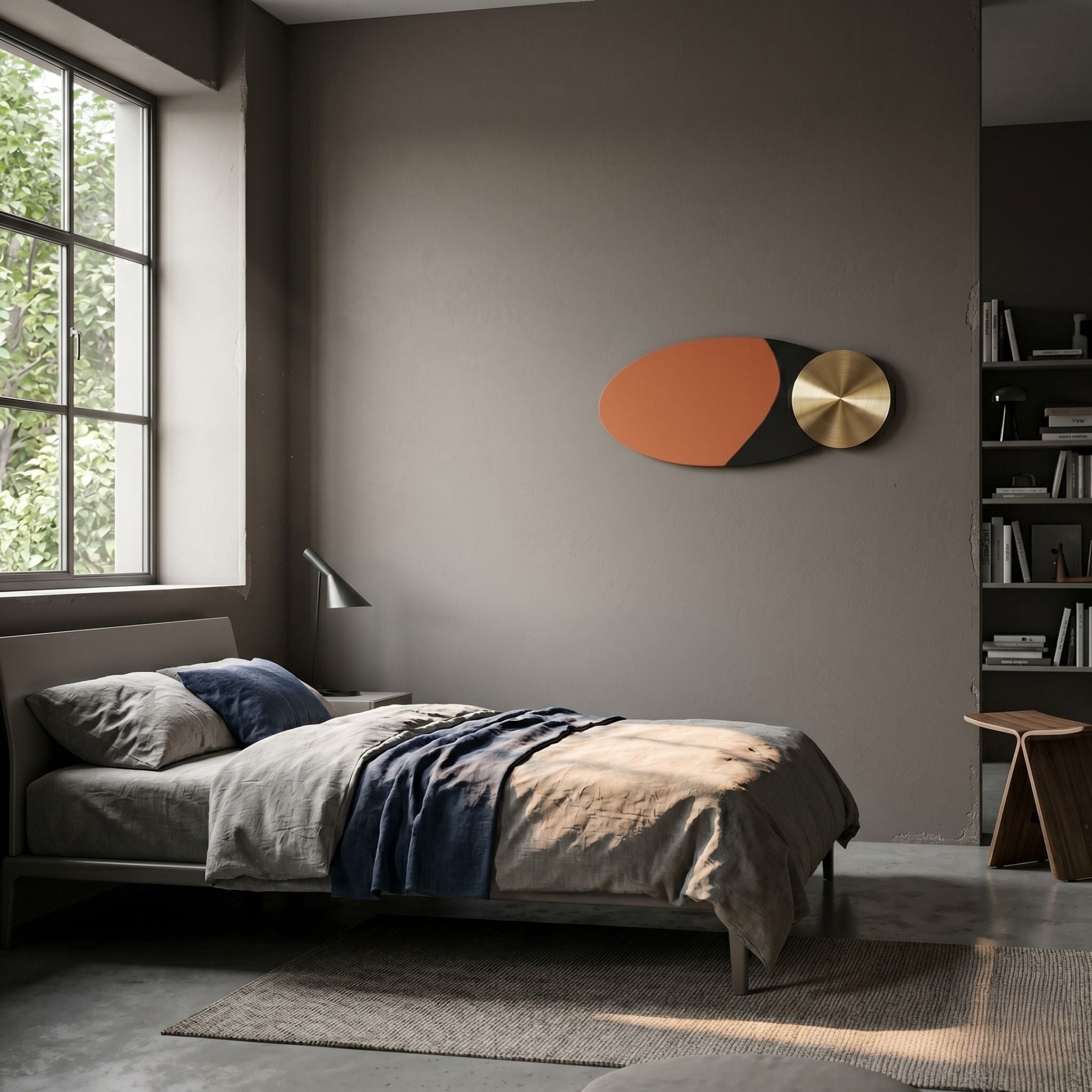 A modern, minimalist bedroom features neutral tones, a neatly made bed, a large window, shelves with books, a small lamp, wooden chair, and is brightened by natural light. Aurelune Amber & Black Gold Metal Disc 3D Wall Art by Giant Sculptures adds style.