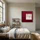 A cozy bedroom features a neatly made bed with beige bedding and a blue blanket by a sunlit window. A bookshelf displays books and decor, while Giant Sculptures’ Loftera Red Grid Sculpted Fabric & Abstract Canvas 3D Wall Art makes a bold statement.