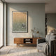 A modern living room with a gray armchair, wooden sideboard, gold lamp, and Giant Sculptures' Lumevara Sandstone Gradient & Chrome Droplet 3D Wall Art on a muted green wall. Sunlight pours through large windows onto a light patterned rug.