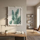 A modern room features a wooden desk, lamp, and books in front, with Giant Sculptures' Verdantia II Green Palm Leaf Textured 3D Wall Art as stylish botanical decor. Sunlit shelves and a chair appear in the background.