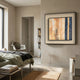 A modern, minimalist bedroom with neutral walls, a neatly made bed, a gray chair, bookshelf, and the Terralume Sand & Indigo Linear Textured Framed Wall Art by Giant Sculptures hanging above. Natural light streams in through a tall window.