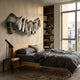 Vellun Wave Graphite Flow 3D wall art with folded black-and-white striped ribbon form mounted above a wooden bed with grey linen bedding and bookshelf.