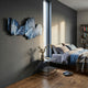 Vellun Wave Midnight Blue Sculptural 3D Wall Art by Giant Sculptures mounted on a dark grey bedroom wall above a nightstand beside a linen-dressed bed.