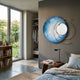 Aurelios Ice Blue Crystal Porcelain & Gold Orbit 3D Wall Art by Giant Sculptures mounted on a grey bedroom wall beside a bed, side table, and garden window.
