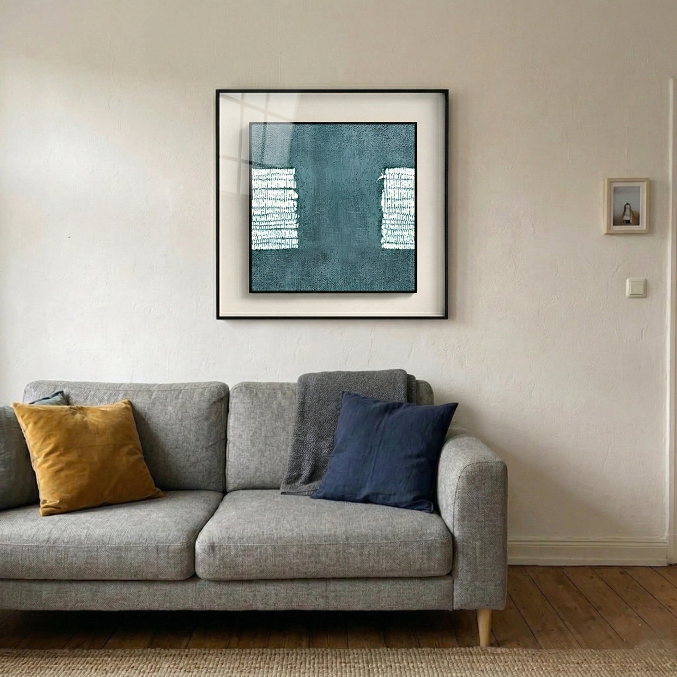 Tracera Teal Block Abstract Textured Framed Wall Art by Giant Sculptures displayed above a grey sofa in a living room, showing deep teal hand-painted surface with white textured blocks in a matte black frame.