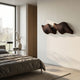 Aeravox Dark Brown Waveform Sculptural 3D Wall Art with layered timber slats mounted on a white bedroom wall above a bed with charcoal linens.