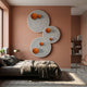 Orbiora Orange Orb 3-Panel Concentric Sphere 3D Wall Art by Giant Sculptures displayed above a grey bed on a terracotta bedroom wall with bookshelves.