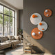 Orbiora Orange & White Orb 4-Panel Concentric Sphere 3D Wall Art displayed on a grey wall in a modern living room with a beige sofa and side table.