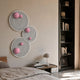 Orbiora Pink Orb 3-Panel Concentric Sphere 3D Wall Art by Giant Sculptures displayed above a bedside table with lamp, beside a dark bookshelf in a bedroom.