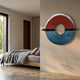 Zenithra Red & Blue Horizon Circular 3D Wall Art by Giant Sculptures mounted on a beige bedroom wall beside a wooden bed with grey linens.