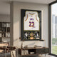 Legends LeBron James #23 Lakers Jersey Framed Wall Art mounted on a neutral wall above a wooden console with books, beside a leather chair and window.