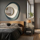 Orrana Blue & White Organic Round Mirror 3D Wall Art by Giant Sculptures displayed above a wooden headboard in a modern bedroom with grey linens and a bedside lamp.