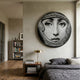 Lunoria Ornate Frame Face Round Wood Embossed Wall Art by Giant Sculptures mounted above a walnut nightstand in a bedroom with grey linen bedding and bookshelf.