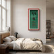 Cavendor Pipe & Cigar Green Framed Wall Art with red border displayed above a bed in a minimalist bedroom with linen bedding and a black table lamp.