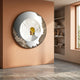 Portara White Cloister Illusion Round 3D Wall Art by Giant Sculptures, mounted on a peach plaster wall beside a built-in bookshelf in a sunlit modern interior.