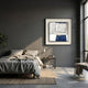 Aerolith Blue & Ivory Abstract Textured Framed Wall Art with navy shapes on ivory texture, displayed above a nightstand in a grey-walled bedroom.