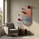 Virellon Rose Gradient 3D Wall Art by Giant Sculptures, oval striped panel with red and silver metal balls, displayed above a grey armchair and walnut side table.