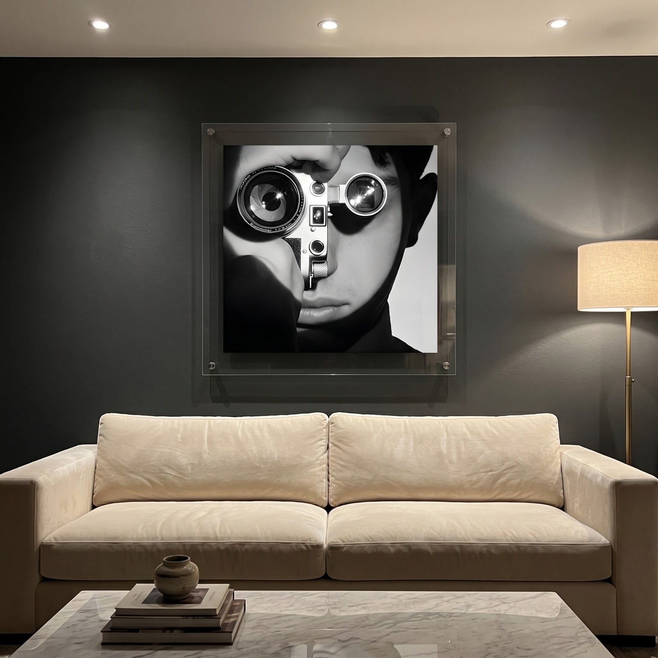 CineLuxe Vintage Camera Boy Black & White Portrait Wall Art by Giant Sculptures, acrylic print of a close-up face holding a vintage camera, mounted on a dark wall above a cream sofa in a modern living room.