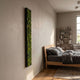 Verdura Vertical Green Moss Strip 3D Wall Art by Giant Sculptures, a tall black-framed preserved moss panel mounted on a light wall beside a wooden bed.
