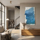 Avarin Sky Blue Wave Swirl Acrylic Tile 3D Wall Art by Giant Sculptures mounted above a wooden sideboard in a modern living room with armchair and bookshelf.