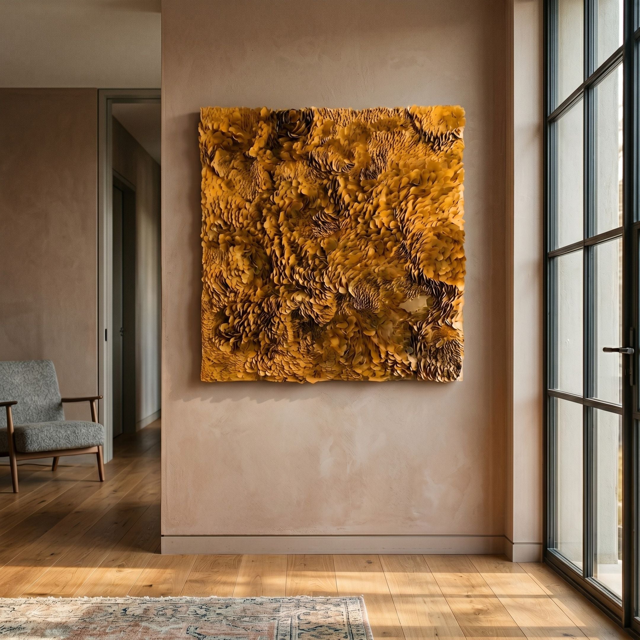 Auralith Ochre Layered Leather 3D Wall Art by Giant Sculptures, a square panel of densely overlapping ochre petals mounted on a warm beige hallway wall beside a grey armchair and tall windows.