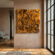 Auralith Ochre Layered Leather 3D Wall Art by Giant Sculptures, a square panel of densely overlapping ochre petals mounted on a warm beige hallway wall beside a grey armchair and tall windows.