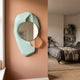 Ravira Aqua & Peach Sculptural Acrylic Mirror by Giant Sculptures mounted on a terracotta hallway wall beside a bedroom with grey bedding and shelving.