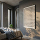 Parella Black Slit Disc Grid Acrylic 3D Wall Art by Giant Sculptures mounted on a grey bedroom wall beside a bed, doorway, and potted plant.