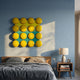 Poplux Grid Yellow & Teal Dome Acrylic 3D Wall Art by Giant Sculptures mounted above a wooden bed with grey linens and a bedside table on a blue wall.