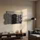 Strialux Flow Veil 3D wall art with wavy black-and-white acrylic stripes on grey leather, displayed above a wooden console with books, vase and floor lamp.