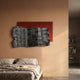 Strialux Flow Veil Red Leather & Acrylic 3D Wall Art with black-and-white striped veil over a red panel, mounted above a bed in a warm terracotta bedroom.