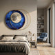 Giant Sculptures Solvata Sapphire Orbit & Metal Ring 3D Wall Art with textured blue disc, silver core and gold rings above a bed beside a blue armchair.