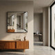 Quadria Single Panel Square Wall Mirror by Giant Sculptures with a slim black frame, mounted above a mid-century walnut sideboard with a vase of dried pampas.