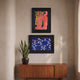Ardensir Pink Cat & Blue Ripple 2-Set Framed Wall Art by Giant Sculptures displayed on a textured beige wall, featuring a pink cat painting above a blue ripple print in ornate black frames, styled above a walnut sideboard with a snake plant.