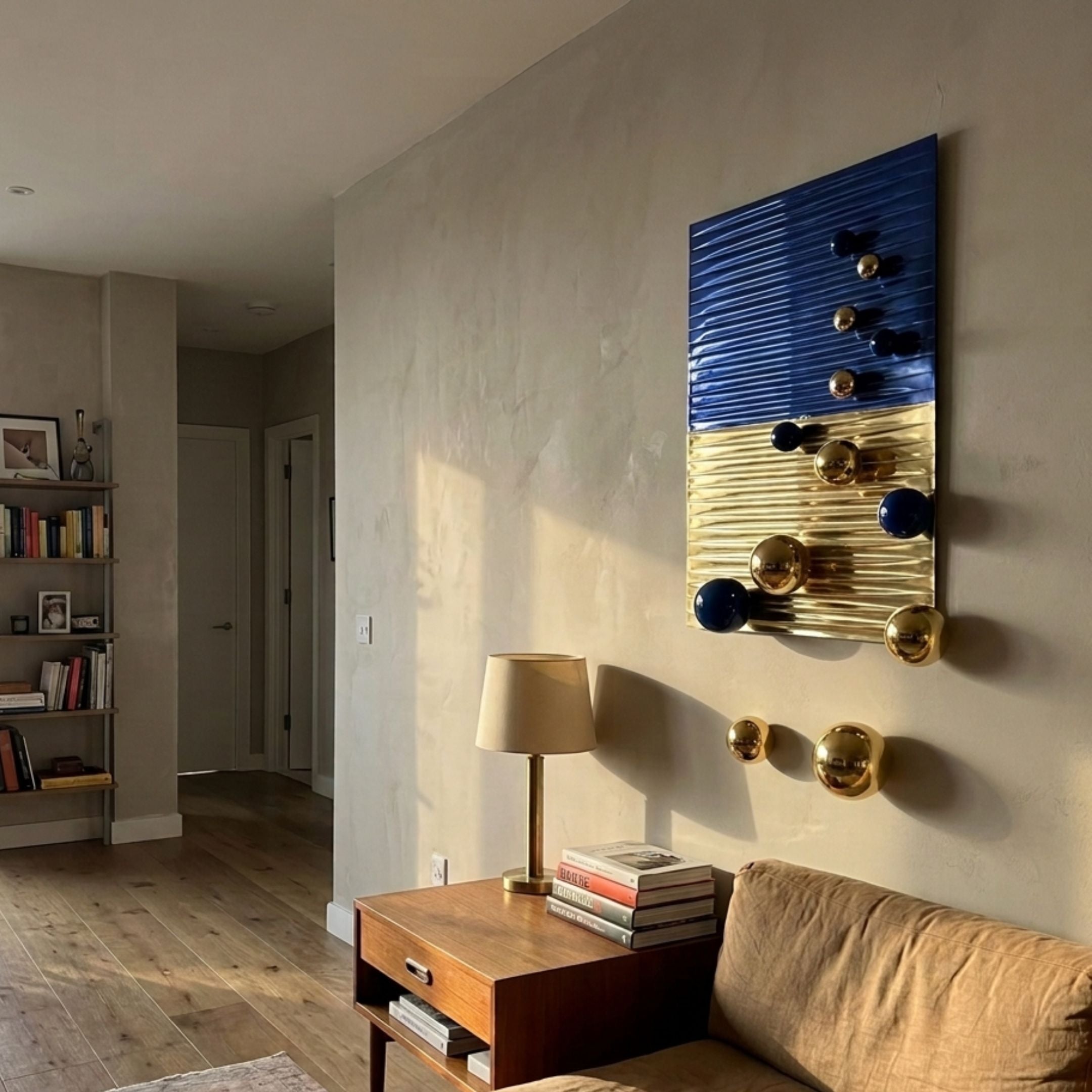 Orbentra Dual-Tone 3D Wall Art by Giant Sculptures mounted in a living room above a teak side table, with ribbed cobalt blue and polished gold halves and protruding metal ball accents.