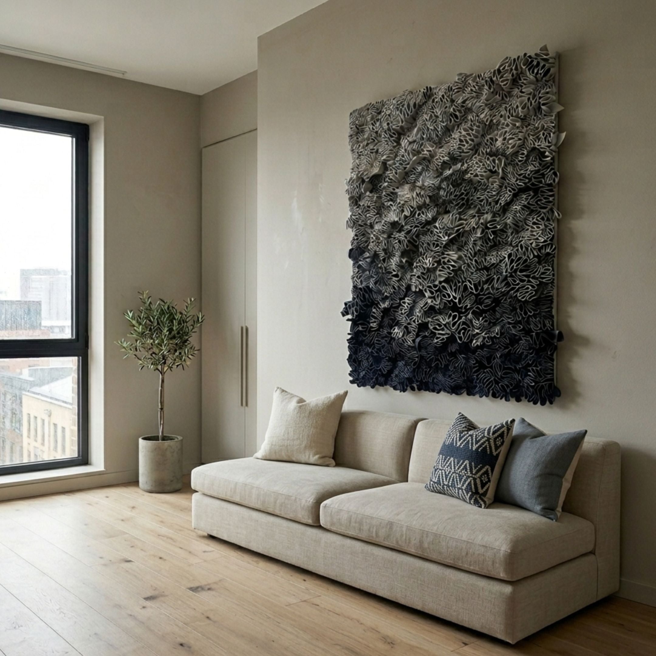 Liora Blue Ombre Ribbon Leather 3D Wall Art by Giant Sculptures, mounted above a beige sofa in a modern living room with an olive tree and window.