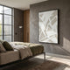 Deralin Taupe Angled Abstract 3D Carving Wall Art in a black frame displayed on a grey concrete wall above a linen-dressed bed in a modern bedroom.