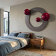 Celestara Grey Round 3D Wall Art by Giant Sculptures mounted above a wooden bed with blue linens, featuring three glossy red metal spheres on a grey ring.