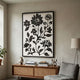 Florentia III Black & White Wood Carving 3D Wall Art by Giant Sculptures displayed above a mid-century cane sideboard with books, vases, and a grey armchair.
