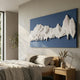 Riftline Panorama Blue Wood Carving 3D Wall Art mounted above a wooden bed with linen bedding, showing white carved glacial form on deep blue panel.